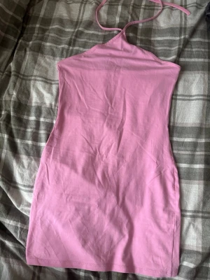 Rosa halterneck kortklänning - Säljer en rosa halterneck klänning med kort längd och tight passform. Klänningen är ärmlös och har en enkel design utan mönster eller detaljer. Materialet känns som mjuk bomull, perfekt för varma dagar. Okänt märke och storlek men tror att den är från hm str S. 