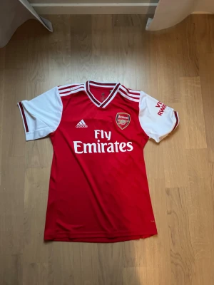Arsenal tröja - Bilderna visar en röd och vit Arsenal fotbollströja från Adidas med tryck 'Fly Emirates' och spelarnamn 'Lacazette' samt nummer 9 på ryggen. 