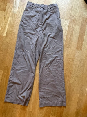 Beige wide kostymbyxor strl 36 - Snygga beige kostymbyxor med breda ben och klassisk midja. Byxorna har hällor för bälte och diskreta fickor bak. Materialet är mjukt och känns som bomull, perfekt för en chill och stilren look.