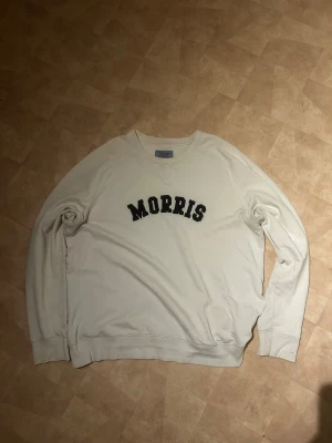 Vit sweatshirt från Morris Company XL - Säljer en vit sweatshirt från Morris Company i storlek XL. Tröjan har klassisk rund hals och svart tryck med MORRIS över bröstet. Långa ärmar och ribbade muddar vid hals, ärmslut och nederkant. Perfekt för chill dagar och enkel att matcha med jeans.