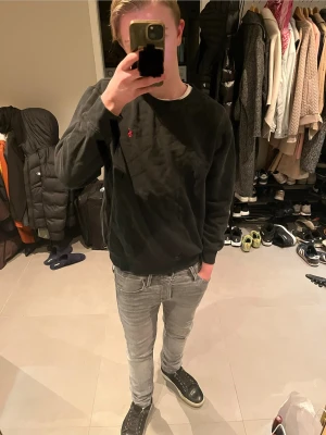 Svart sweatshirt från Polo Ralph Lauren - Svart sweatshirt från Polo Ralph Lauren med klassisk röd broderad logga på bröstet. Tröjan har rund hals, ribbade muddar och är tillverkad i mjuk bomull. Passformen är normal och den har långa ärmar. Perfekt för chill dagar och enkel att matcha med jeans.