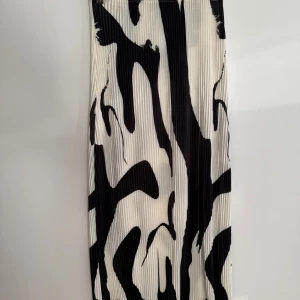 Plisserad långkjol med svartvitt mönster - Säljer en plisserad långkjol i storlek XS med ett  svartvitt mönster. Kjolen är gjord av 100% polyester och har en flowy känsla. Har aldrig använts då den är väldigt genomskinlig. 