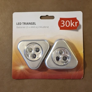 LED Triangel - LED Triangel-lampor, 2-pack, drivs med 3 x AAA-batterier (ej inkluderat). Varje lampa har 6 LED, diameter 70mm, effekt 0.5W och ljusflöde 10lm. Förpackningen har mindre skav och veck men produkten är ny och oanvänd.