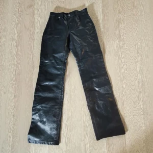 Svarta glansiga byxor från Weekday - Säljer ett par svarta glansiga byxor från Weekday i storlek 36. Byxorna har raka ben och klassisk femficksmodell med knapp och dragkedja. Materialet har en snygg glansig finish som sticker ut och ger en cool look.