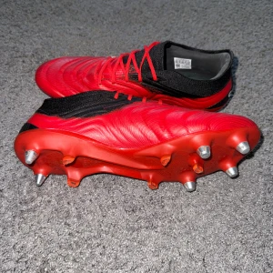 Adidas Copa 20.1 röda fotbollsskor - Säljer ett par Adidas Copa 20.1 fotbollsskor i rött med svarta och vita detaljer. Skorna har snörning, låg profil och metall-dobbar för extra grepp på planen. Ovandelen är tillverkad i skinn och syntet med en strumpliknande svart krage för skön passform. 
