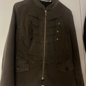 Mörkgrön jeansjacka med dragkedja - Snygg mörkgrön jeansjacka med raka linjer och coola dekorativa knappar framtill. Jackan har dragkedja, två fickor med knappstängning och lång ärm. Perfekt för dig som gillar en stilren look med lite edge. Inhandlades för 699 kr - säljer för billigare!