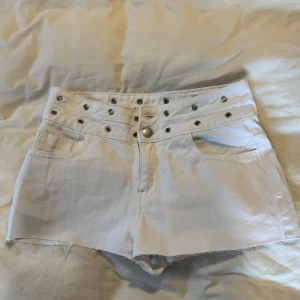 Vita högmidjade shorts med nitar - Snygga vita shorts med hög midja och coola silverfärgade nitar längs linningen. Rå kant nertill för en edgy vibe och klassiska fickor både fram och bak. Perfekta för dig som vill sticka ut lite extra i sommar.