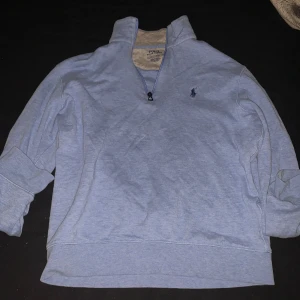 Ljusblå half zip tröja Äkta Polo Ralph Lauren - Ljusblå långärmad tröja från Polo Ralph Lauren med klassisk broderad logga på bröstet. Tröjan har en snygg half zip-dragkedja och hög krage. Tillverkad i mjuk bomull, perfekt för lager-på-lager och chill stil.