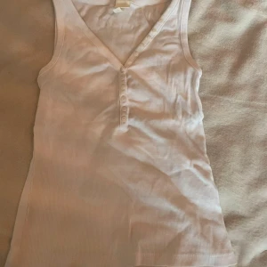 Vit ribbad linnetopp från H&M - Säljer en vit ribbad linnetopp från H&M med v-ringning och dekorativa knappar framtill. storlek Xs