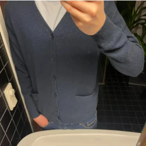 Mörkblå kashmirkofta Emilio Tucci - Säljer en riktigt mjuk och lyxig mörkblå kofta från Emilio Tucci i 100% kashmir. Koftan har v-ringning, knäppning framtill med fem knappar och två fickor. Perfekt för dig som vill ha en stilren och bekväm look. Perfekt nu till hösten och vintern. Kan styla med en skjorta eller t shirt under. Tröjan är i bra skick och har inga defekter. Passar någon som är mellan 180-190 beroende på vikt.