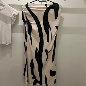 Beige långkjol med svart zebramönster - Cremevit långkjol med svart mönster och snygg rynkdetalj i sidan. Kjolen har en fin passform och är gjord i ett mjukt bomullsliknande material. Perfekt för dig som vill sticka ut med ett mönster och ändå hålla det stilrent.