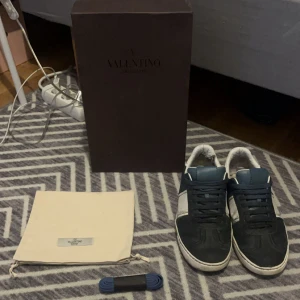 Valentino Flycrews - Snygga Valentino Garavani sneakers i svart och vitt skinn med klassisk låg profil och rund tå. Skorna har svarta snören och medföljer extra blå skosnören samt dustbag och originalkartong. Perfekt för dig som gillar exklusiva och stilrena sneakers.