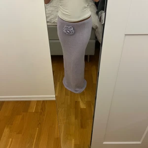 Virkad Maxi kjol - Säljer denna helt oanvända maxi kjolen i ett virkat bekvämt material med en stor insydd ros på. Den är köpt från Na-kd gamla kollektion. Färgen är en ljus lila. Kjolen är ganska tjock i material och även i strech.