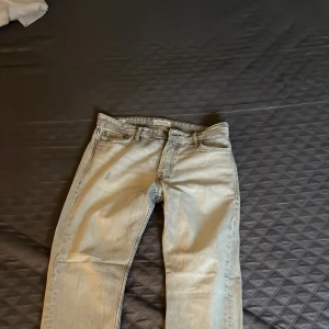 Ljusgrå jeansbyxor storlek 30/30 - Snygga ljusgrå jeansbyxor i klassisk femficksmodell med raka ben och normal passform. Byxorna har detaljerade sömmar och en diskret läderpatch baktill i midjan. Perfekt för dig som gillar stilrena och neutrala färger.