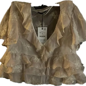 Beige blommig blus med volanger - Säljer en romantisk beige blus från Zra i storlek M. Blusen har broderade blommor, volanger och v-ringad hals. Materialet är lätt och transparent med korta ärmar. Perfekt för dig som gillar feminina detaljer och en luftig känsla. ord pris: 390 sek, säljer för 325 på grund av att den är nyköpt.