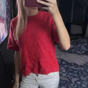 Röd stickad kortärmad tröja från Gina Tricot - Säljer en röd stickad tröja med korta ärmar och rund hals. Tröjan har en avslappnad passform och är perfekt för lager-på-lager. Enkel och stilren design som funkar till många outfits.