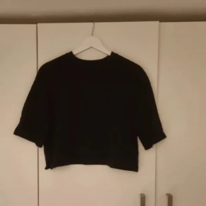 Svart croppad topp från Zara - Svart croppad topp från Zara med korta ärmar och rund hals. Toppen har en enkel och stilren design med små slitsar i sidorna nedtill. Perfekt för dig som gillar minimalistisk stil och vill ha en basic topp i garderoben.