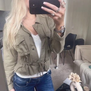 Militärgrön höstjacka - Snygg olivgrön utilityjacka med fyra stora fickor framtill och snörning i midjan för en schysst passform. Jackan har knappar och är långärmad, perfekt att slänga på sig över en topp. Passar dig som gillar en avslappnad men trendig stil.