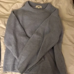 Ljusblå stickad tröja från Gina Tricot - Supermysig ljusblå stickad tröja från Gina Tricot i ullblandning. Tröjan har rund halsringning, ribbade muddar och en relaxed fit som ger en chill vibe. Perfekt att slänga på sig när det är kallt ute.