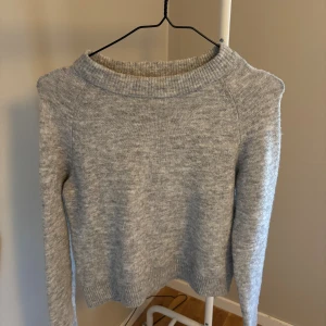 Grå stickad tröja från Vero Moda - Mysig grå stickad tröja från Vero Moda i storlek XS. Tröjan har en klassisk rund halsringning, ribbade muddar och lång ärm. Perfekt för lager-på-lager och enkel att matcha med jeans eller kjol.