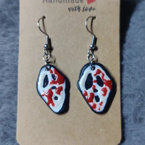 Scream-inspirerade örhängen i polymerlera - Unika örhängen med Scream-mask motiv, handgjorda i polymerlera. Svart bas med vit och röd färg som ger en blodig effekt. Perfekt för dig som gillar skräck och vill sticka ut med coola accessoarer. Krokar i metall.