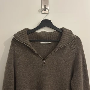 Brun ulltröja med half zip från A Day's March - Mysig brun stickad tröja från A Day's March i 100% lammull. Tröjan har en bred ribbad krage och en snygg half zip-dragkedja framtill. 