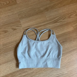 Ljusgrå ribbad linnetopp från ICIW - Säljer en ljusgrå ribbad linnetopp från ICIW med smala korsade axelband i ryggen. Toppen är stretchig och har en croppad passform, perfekt för träning eller chill. Diskret ICIW-logga framtill. Superskön och stilren design!