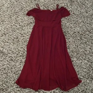 Röd långklänning - Superfin röd långklänning med axelband, volang och dragkedja i ryggen. Klänningen har en stilren men festlig look och passar perfekt till finare tillfällen. Endast använd en gång.