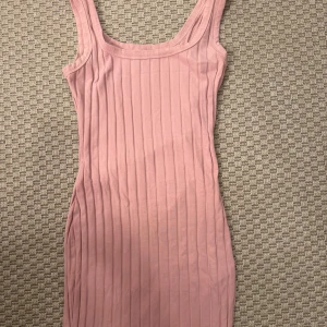 Rosa ribbad kortklänning - Säljer en söt rosa kortklänning med ribbad struktur och ärmlös design. Klänningen har en rundad halsringning och är figurnära, perfekt för dig som gillar en enkel men snygg look. Passar dig som vill ha något bekvämt och stilrent.