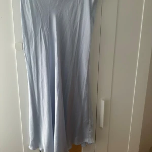 Ljusblå långkjol i satin - En stilren och flowy ljusblå långkjol i satinliknande material. Kjolhar en enkel och elegant design med mjukt fall och utan synliga detaljer. Perfekt för dig som gillar minimalistisk stil och vill ha något som känns både luftigt och classy.