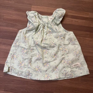 Blommig ljusgrön klänning - Supersöt ljusgrön kortklänning från Newbie med blommigt mönster i pastellfärger. Storlek 62 (2-4mån) och sparsamt använd helt utan anmärkningar. Knappar i ryggen.