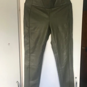 Olivgröna skinnleggings - Snygga olivgröna leggings i skinnimitation med hög midja och smal passform. Perfekta för att lyfta vilken outfit som helst med sin coola look och trendiga färg. Passar dig som gillar att sticka ut och vill ha något annorlunda i garderoben.