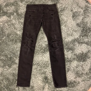 Hm jeans - Säljer ett par svarta skinny jeans med snygga slitningar över knäna och detaljerade revor. Jeansen har klassisk femficksdesign och är i stretchigt denimtyg som sitter tight hela vägen ner. Perfekta för dig som gillar en edgy och trendig look.