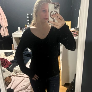 Svart v-ringad stickad tröja - En svart stickad tröja med v-ringning och långa ärmar. Tröjan har en enkel och stilren design som passar perfekt till jeans. Mjuk och skön att bära, med en lite loose passform.