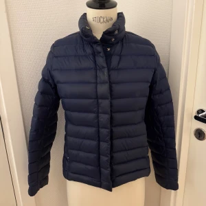 Polo Ralph Lauren marin dunjacka - Snygg mörkblå dunjacka från Polo Ralph Lauren med broderad logga på bröstet. Ca stl 12-14 år men hon som haft den är 15 år och brukar ha xs. Jackan knappar och dragkedja. Yttertyget är i nylon och fodret består av vitt ankdun för extra värme. Perfekt för kalla dagar. En liten lagning på jackan -därav priset. Lagningen syns inte alls faktiskt. Men på sista bilden har jag ljusat upp fotot så du kan se. Kan hämtas på Hägerstensåsen i Stockholm 🌸