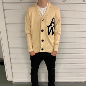 Beige kofta från Jack & Jones L - Säljer en beige kofta från Jack & Jones i storlek L. Koftan är i 100% bomull, har stora svarta knappar och en broderad svart AW-logga på bröstet. Den har ribbade muddar och en klassisk krage. Perfekt för lager-på-lager och chill stil.