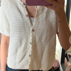 Vit stickad blus från Gina Tricot - Supersöt vit stickad blus från Gina Tricot i storlek XL. Den har korta ärmar, v-ringning och knappar framtill. Perfekt till sommaren med sitt luftiga material och snygga struktur. Enkel att styla med jeans eller kjol för en chill look.
