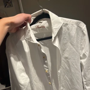 Vit henley-skjorta från Stenströms - Snygg vit henley-skjorta från Stenströms med klassisk krage och guldfärgade knappar. Skjortan är långärmad och tillverkad i mjuk bomull som känns skön mot huden. Perfekt för dig som gillar stilrena och enkla plagg med en clean look.