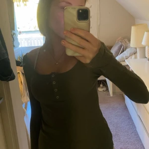 Olivgrön ribbad långärmad topp Pieces - Olivgrön långärmad topp från Pieces med ribbad struktur och rund halsringning. Toppen har knappdetaljer framtill och är figurnära i modellen. Perfekt att styla med jeans eller kjol för en enkel men snygg look.