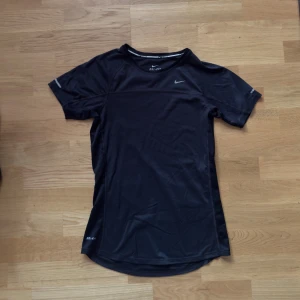 Svart Nike Dri-Fit t-shirt - Svart sportig t-shirt från Nike med Dri-Fit-teknologi. T-shirten har korta ärmar, rund halsringning och en liten Nike-logga på bröstet. Perfekt för träning och aktiva dagar.
