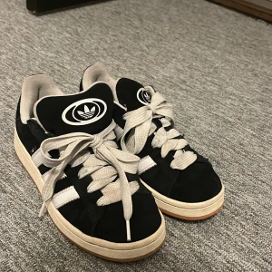 Svarta Adidas sneakers strl 38 - Svarta adidas campus. Väl använda men i bra skick. Med nya skosnören hade dem nästan sett ut som nya. Storlek 38 2/3.
