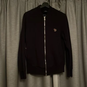 Mörkblå tröja från Paul Smith med dragkedja - Mörkblå tröja från Paul Smith med hel dragkedja framtill och liten broderad logga på bröstet. Klassisk modell med ribbade muddar och krage. Perfekt för lager-på-lager och snygg till både jeans och chinos. Nypris: 1800kr.