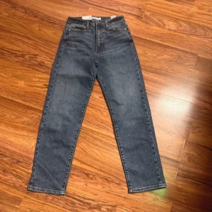 Blå mom fit jeans straight XS/30 - Snygga blå mom fit jeans från C i rak modell. Hög midja och klassisk femficksdesign. Jeansen är i bomull och har en cool tvättad look med orangea sömmar. Perfekta för dig som gillar en avslappnad men trendig stil.