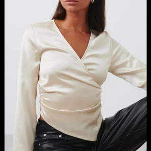 Champagnefärgad omlottopp från Gina  - Säljer en champagnefärgad omlottopp från Gina Tricot i glansig satin. Toppen har lång ärm, v-ringning och snygg omlottdetalj framtill som ger en cool siluett. Perfekt för dig som gillar stilrena och trendiga plagg med lite extra lyxig känsla. Använd en gång! (Obs, första bilden är inte min men den ser ut så på!) 💛