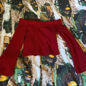 Röd offshoulder ribbad topp - Säljer en snygg röd offshoulder topp med långa utsvängda ärmar. Toppen är ribbad och croppad, vilket ger en trendig look. Perfekt att styla med höga jeans eller kjol. Materialet känns mjukt och stretchigt.