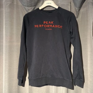 Svart Peak Performance sweatshirt - Svart sweatshirt från Peak Performance med röd broderad logga på bröstet. Storlek 170 utan tecken på användning.