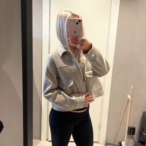 Snygg kort ”kappa” - Säljer en as snygg  beige kort ”kappa”, två stora fickor framtill. Jackan är kort som croppad och har långa ärmar samt knappar längs framsidan. Materialet känns mjukt och har en ull-liknande look, perfekt för lager på lager. Enkel och clean stil som funkar till allt. Skriv innan köp! ❤️❤️