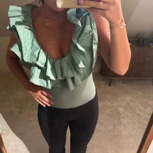 Mintgrön volang body med djup urringning - Säljer en mintgrön body med stora volanger runt halsringningen och axlarna. Aldrig använd och väldigt stretchig så passar fler storlekar!🩷
