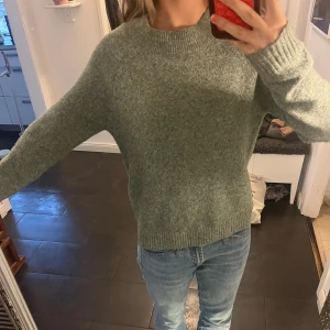 Grön stickad tröja med rund hals - Mysig grön stickad tröja med rund halsringning och ribbade muddar vid ärmslut och nederkant. Tröjan har en klassisk, enkel design och är perfekt för kyligare dagar. Passformen är normal och ärmarna är långa.💚