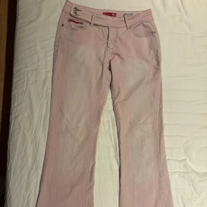 Ljusrosa bootcut jeans Blue Collection - Säljer ett par ljusrosa jeans från Blue Collection med bootcut passform. Byxorna har dubbla knappar i midjan, klassiska fem fickor och snygga kontrastsömmar på bakfickorna. Perfekta för dig som vill sticka ut med en unik färg och coola detaljer.